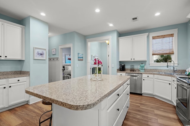 kitchen with sink, a kitchen breakfast bar, a kitchen island, stainless steel appliances, and white cabinets