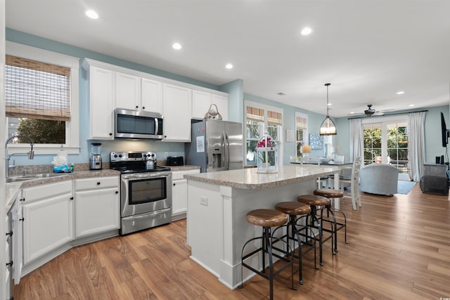 kitchen featuring pendant lighting, stainless steel appliances, a kitchen island, and white cabinets