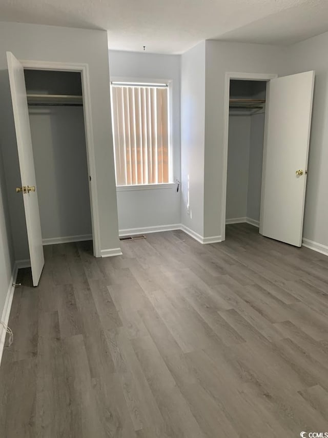 unfurnished bedroom with wood-type flooring and multiple closets