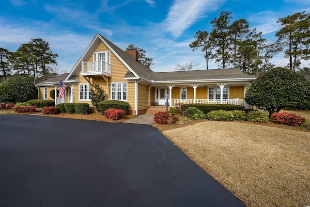 view of front of home with a porch, a chimney, and a balcony