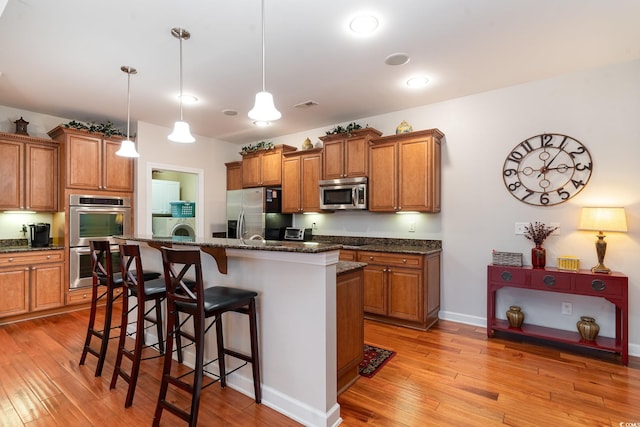 kitchen with hanging light fixtures, a center island with sink, dark stone counters, and appliances with stainless steel finishes