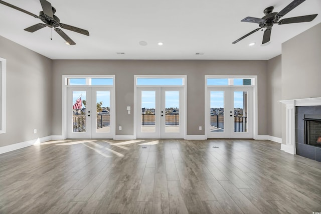 unfurnished living room featuring a tiled fireplace, wood-type flooring, ceiling fan, and french doors