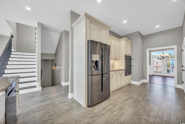 kitchen featuring stainless steel fridge, a chandelier, backsplash, double wall oven, and cream cabinetry