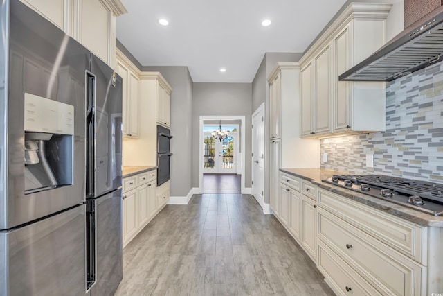 kitchen featuring appliances with stainless steel finishes, backsplash, light hardwood / wood-style floors, cream cabinets, and wall chimney exhaust hood