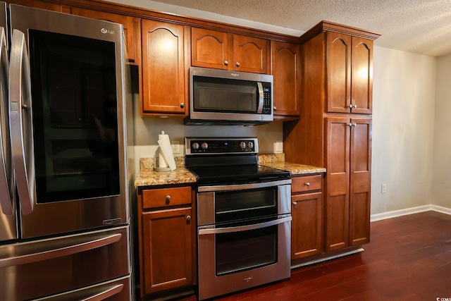 kitchen featuring stainless steel appliances, dark hardwood / wood-style flooring, a textured ceiling, and light stone counters