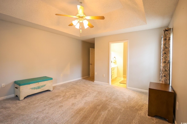 unfurnished bedroom with ensuite bath, ceiling fan, carpet flooring, a tray ceiling, and a textured ceiling