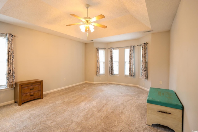 unfurnished room featuring ceiling fan, a raised ceiling, light carpet, and a textured ceiling