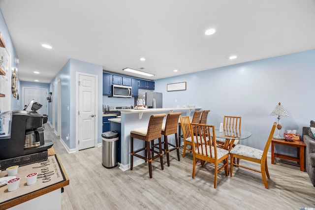 kitchen with appliances with stainless steel finishes, a breakfast bar, blue cabinets, a wood stove, and light hardwood / wood-style floors