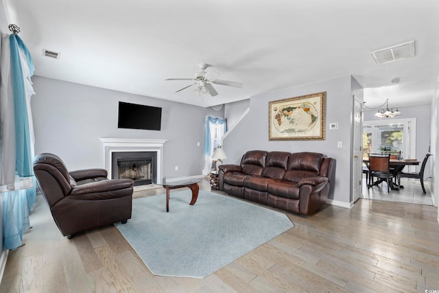 living room featuring ceiling fan with notable chandelier and light hardwood / wood-style flooring