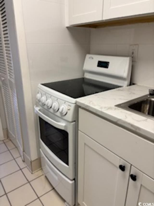 kitchen featuring white cabinets, light tile patterned flooring, light stone counters, and white electric range