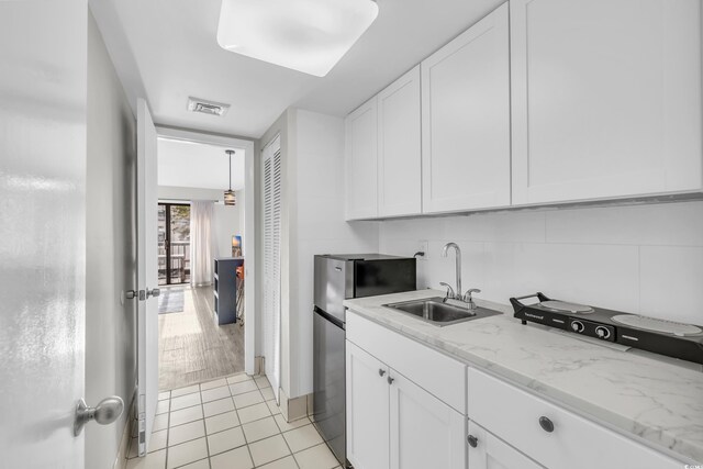 kitchen featuring stainless steel refrigerator, white cabinetry, sink, light tile patterned floors, and light stone counters