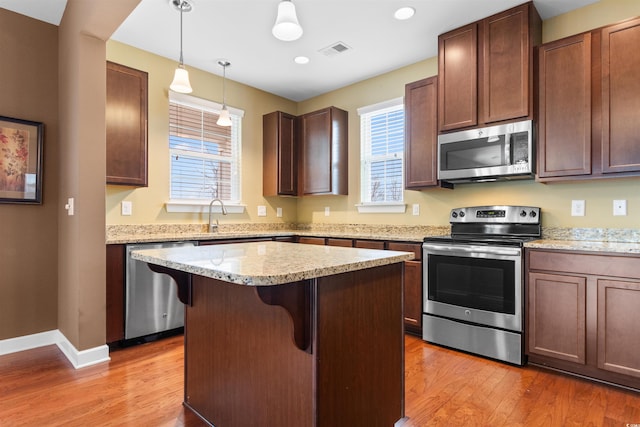 kitchen featuring a kitchen island, appliances with stainless steel finishes, a breakfast bar, pendant lighting, and wood-type flooring