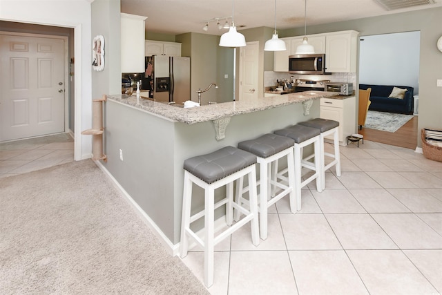 kitchen featuring pendant lighting, appliances with stainless steel finishes, white cabinets, light tile patterned flooring, and kitchen peninsula