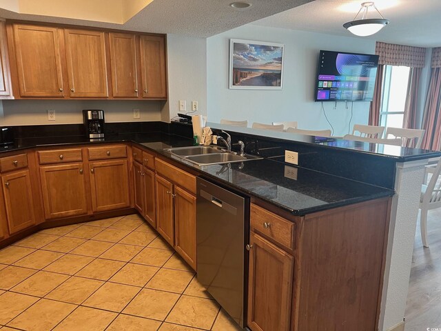 kitchen featuring a peninsula, stainless steel dishwasher, a sink, and brown cabinets