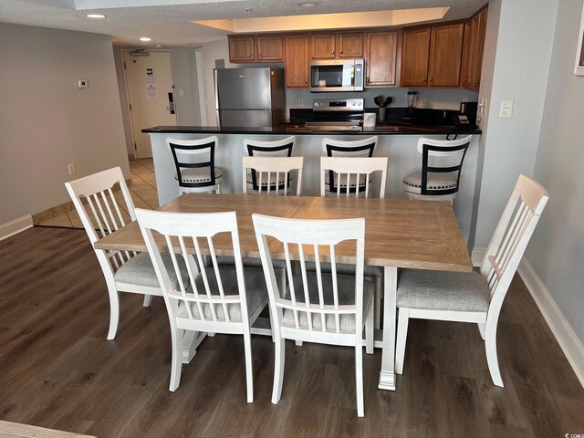 dining space with recessed lighting, a textured ceiling, baseboards, and wood finished floors