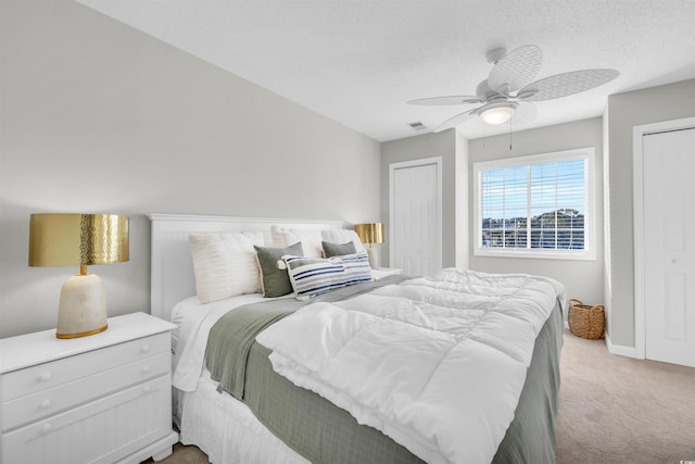 carpeted bedroom with multiple closets, a textured ceiling, and ceiling fan