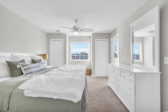 carpeted bedroom with multiple closets, ceiling fan, multiple windows, and a textured ceiling