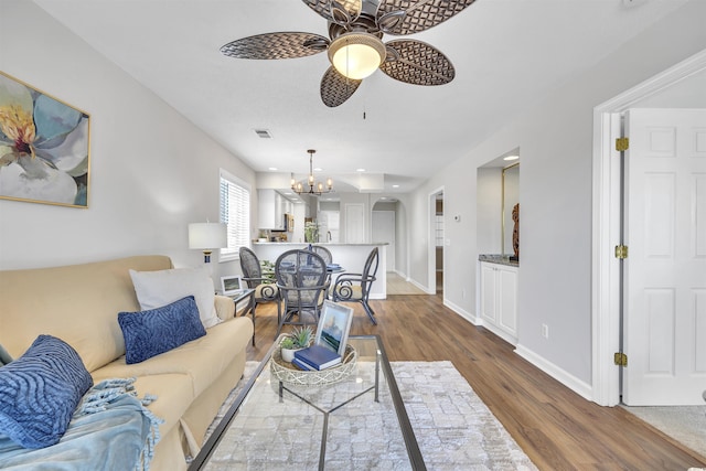 living room featuring ceiling fan with notable chandelier and hardwood / wood-style floors