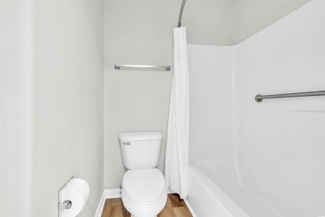 bathroom featuring hardwood / wood-style flooring, shower / bathtub combination with curtain, and toilet