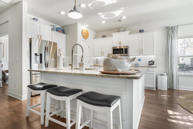 kitchen with dark wood-type flooring, stainless steel appliances, an island with sink, and white cabinets