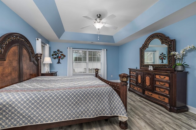 bedroom featuring a raised ceiling, light wood-type flooring, and ceiling fan