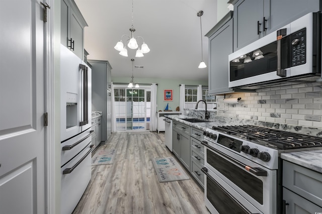 kitchen with sink, gray cabinetry, premium appliances, pendant lighting, and light stone countertops