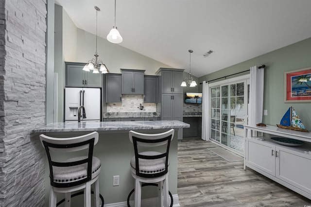 kitchen featuring a breakfast bar, light stone counters, vaulted ceiling, white fridge with ice dispenser, and backsplash