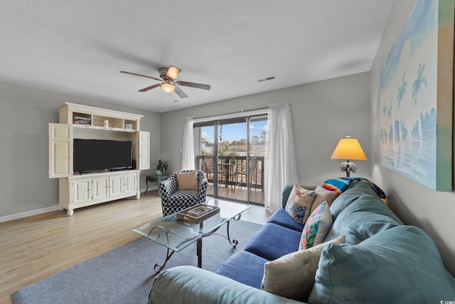 living room with ceiling fan, a textured ceiling, and light wood-type flooring