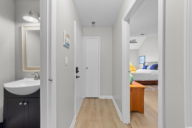 hall with sink, a textured ceiling, and light hardwood / wood-style floors