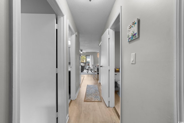 corridor with light hardwood / wood-style floors and a textured ceiling