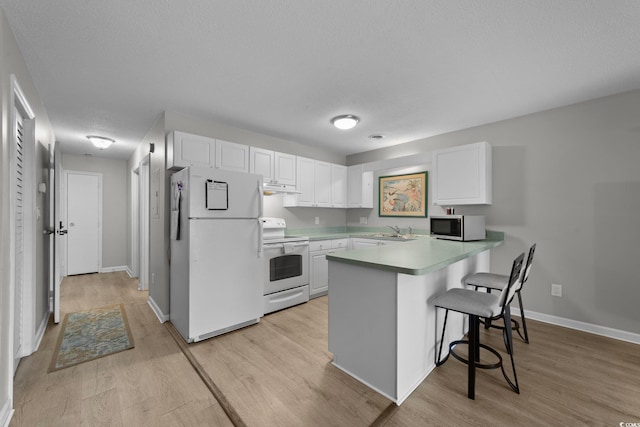 kitchen with sink, white cabinetry, a kitchen breakfast bar, kitchen peninsula, and white appliances