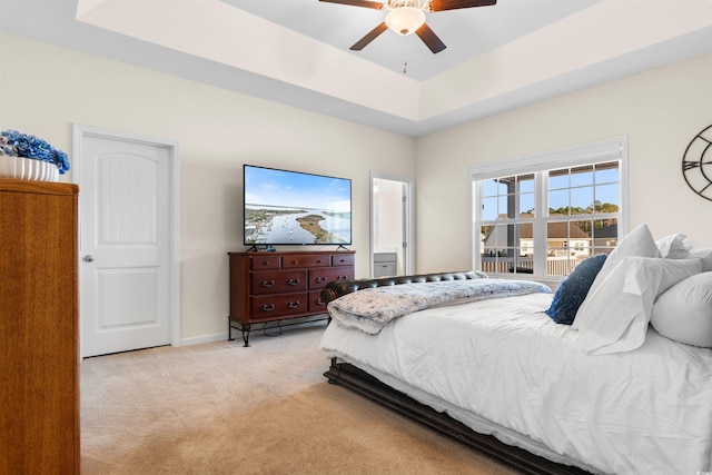 carpeted bedroom with a raised ceiling and ceiling fan