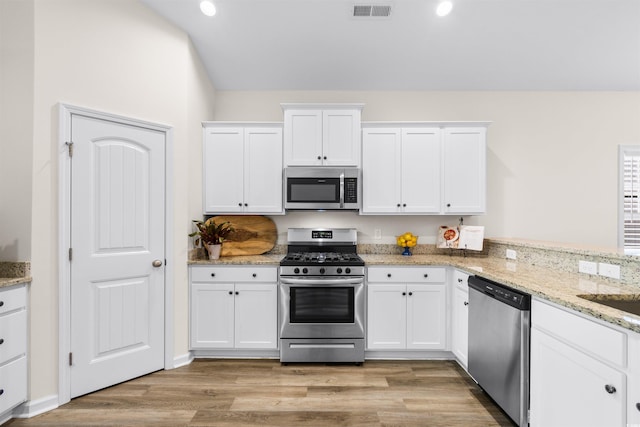 kitchen with light stone counters, light wood-type flooring, kitchen peninsula, stainless steel appliances, and white cabinets