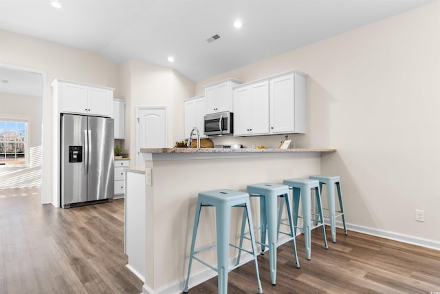 kitchen with stainless steel appliances, white cabinetry, hardwood / wood-style flooring, and a breakfast bar area