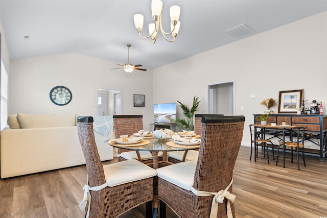 dining space featuring hardwood / wood-style flooring, ceiling fan with notable chandelier, and vaulted ceiling