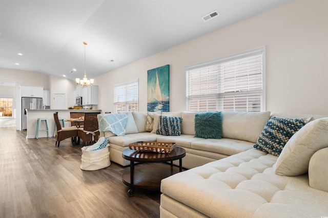 living room with an inviting chandelier, hardwood / wood-style flooring, and vaulted ceiling