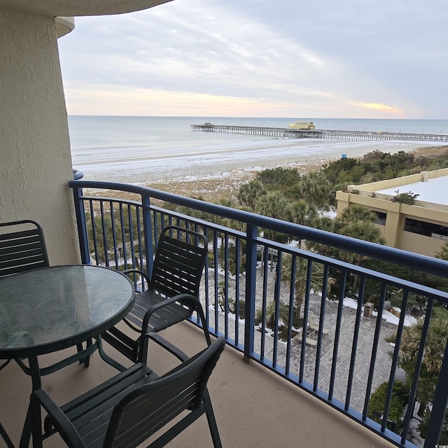 balcony at dusk with a water view and a view of the beach