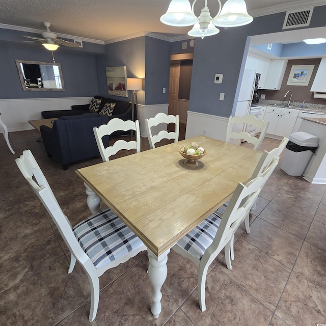 dining space with sink, a textured ceiling, ornamental molding, a notable chandelier, and tile patterned flooring