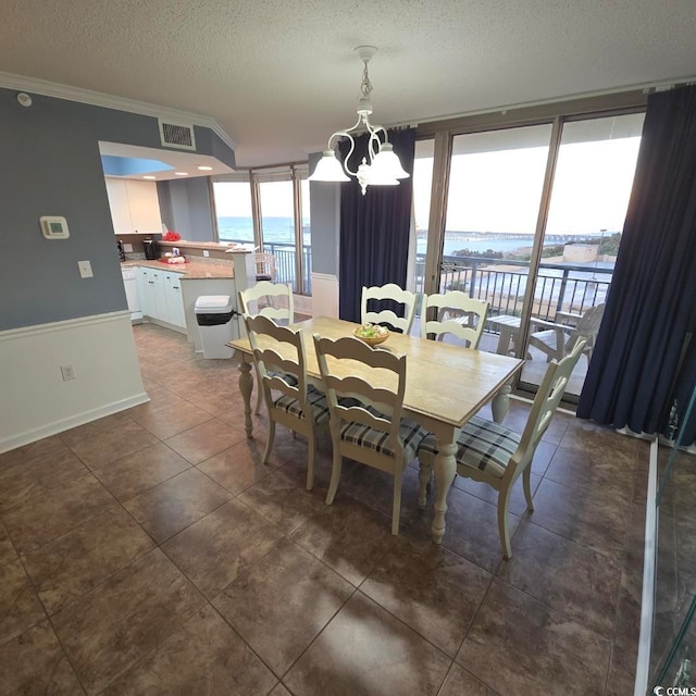 tiled dining area with crown molding, a water view, an inviting chandelier, and a textured ceiling