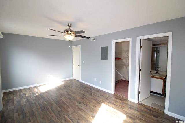 unfurnished bedroom with a spacious closet, dark hardwood / wood-style flooring, electric panel, a closet, and ceiling fan