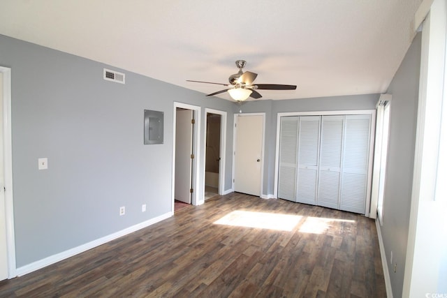 unfurnished bedroom featuring ceiling fan, dark hardwood / wood-style flooring, electric panel, and two closets