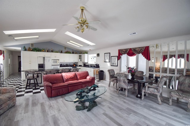 living room featuring ceiling fan, vaulted ceiling with skylight, and light wood-type flooring