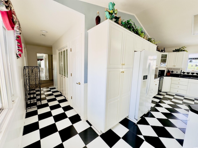 kitchen featuring dishwasher, vaulted ceiling, white fridge with ice dispenser, and white cabinets