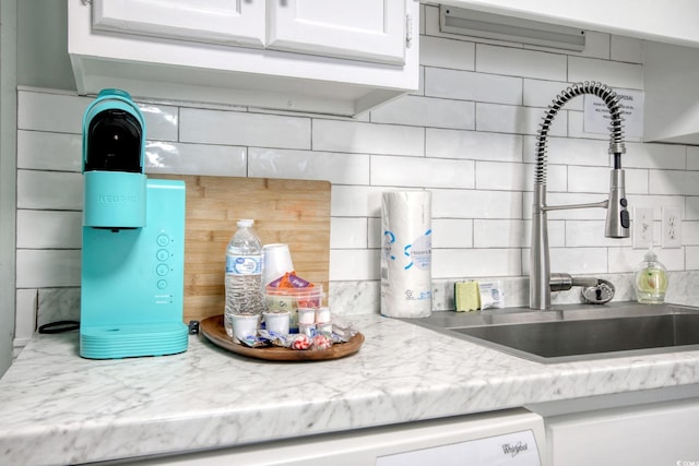 kitchen featuring white cabinetry, backsplash, light stone countertops, and sink