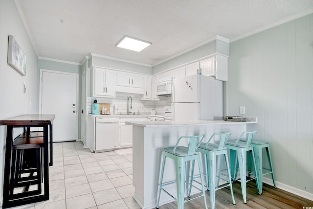 kitchen featuring white cabinetry, sink, a kitchen breakfast bar, kitchen peninsula, and white appliances