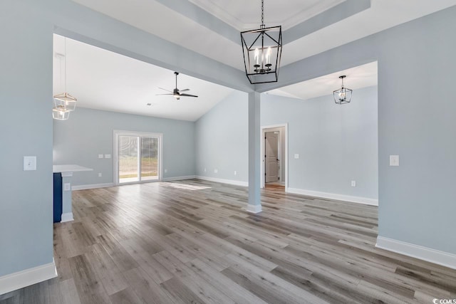 unfurnished living room featuring lofted ceiling, light hardwood / wood-style flooring, a tray ceiling, ornamental molding, and ceiling fan with notable chandelier