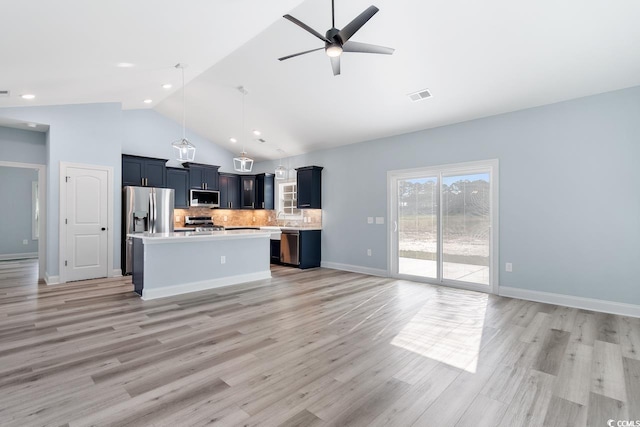 kitchen with appliances with stainless steel finishes, pendant lighting, backsplash, a center island, and light hardwood / wood-style floors