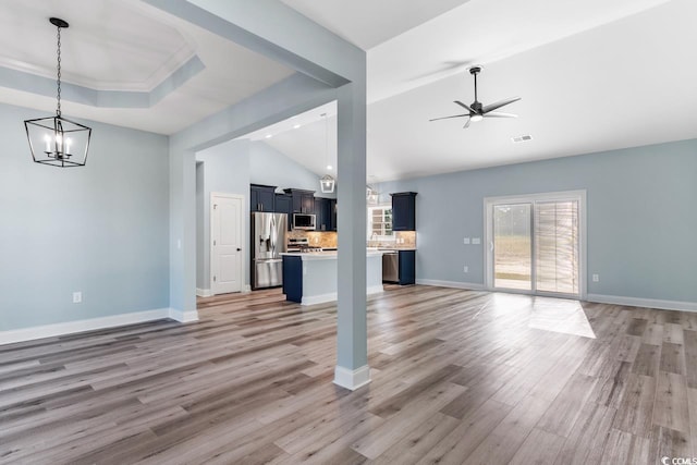 unfurnished living room featuring hardwood / wood-style floors, ornamental molding, ceiling fan with notable chandelier, vaulted ceiling, and a raised ceiling