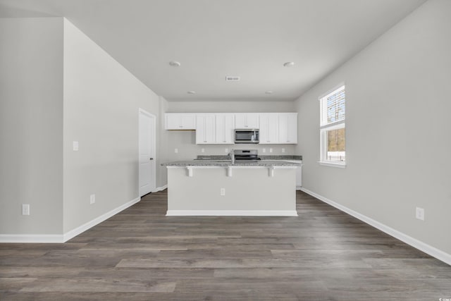 kitchen with stainless steel appliances, light stone counters, an island with sink, white cabinets, and a kitchen bar