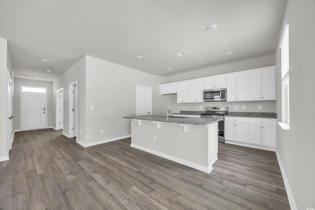 kitchen featuring white cabinetry, appliances with stainless steel finishes, a center island with sink, and dark stone counters